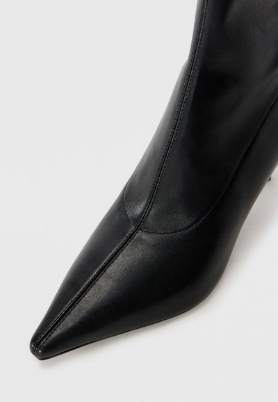 Czarne skórzane botki za kostkę z wydłużonym noskiem, gładką teksturą, minimalnymi detalami szycia i elegancką sylwetką.