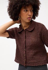 Καφέ κοντομάνικο κάρντιγκαν με υφή, ανοιχτό πλέγμα, γιακά και μπροστινό κλείσιμο με κουμπιά. Διακοσμημένο με στρογγυλά, χρυσά κουμπιά.