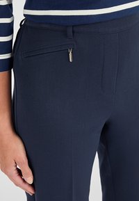Ripresa ravvicinata di una mano appoggiata su pantaloni blu navy con una tasca laterale con zip, abbinati a un top a righe blu e bianche.