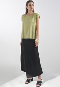 Olivově zelený top s krátkým rukávem, spárovaný s černou maxi sukní. Model má na sobě černé skládací sandály a světlé náramky.