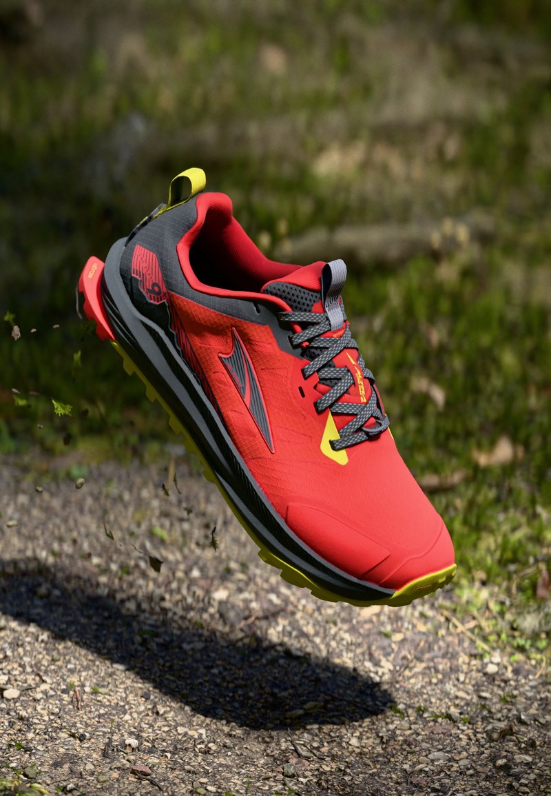 Baskets de course rouges et noires avec une tige texturée, des lacets gris et une touche de jaune. Dotées d'une semelle robuste pour une bonne traction sur diverses surfaces.