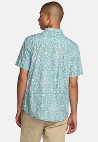 Short-sleeve button-up shirt in teal with white abstract patterns, relaxed fit, and back yoke detail. Lightweight fabric, smooth texture.