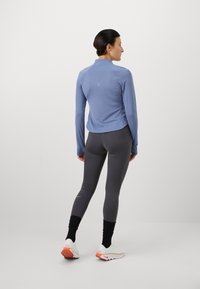 Lichtblauw langärmelig sporttop; grijze aansluitende leggings met textuurpanelen; witte en oranje hardloopschoenen; minimale merkuiting.