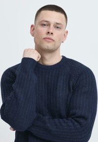 Navy blue ribbed sweater with a round neckline, textured knit, and long sleeves. Fitted silhouette and subtle detailing on cuffs.
