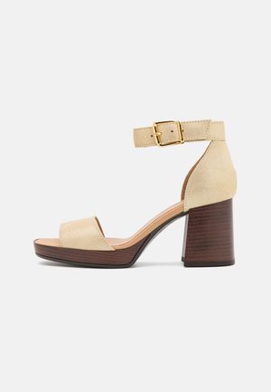 Sandal con apertura sulla punta in suede beige, dotata di una fibbia alla caviglia e tacco in legno marrone, con una texture liscia e un leggero plateau.