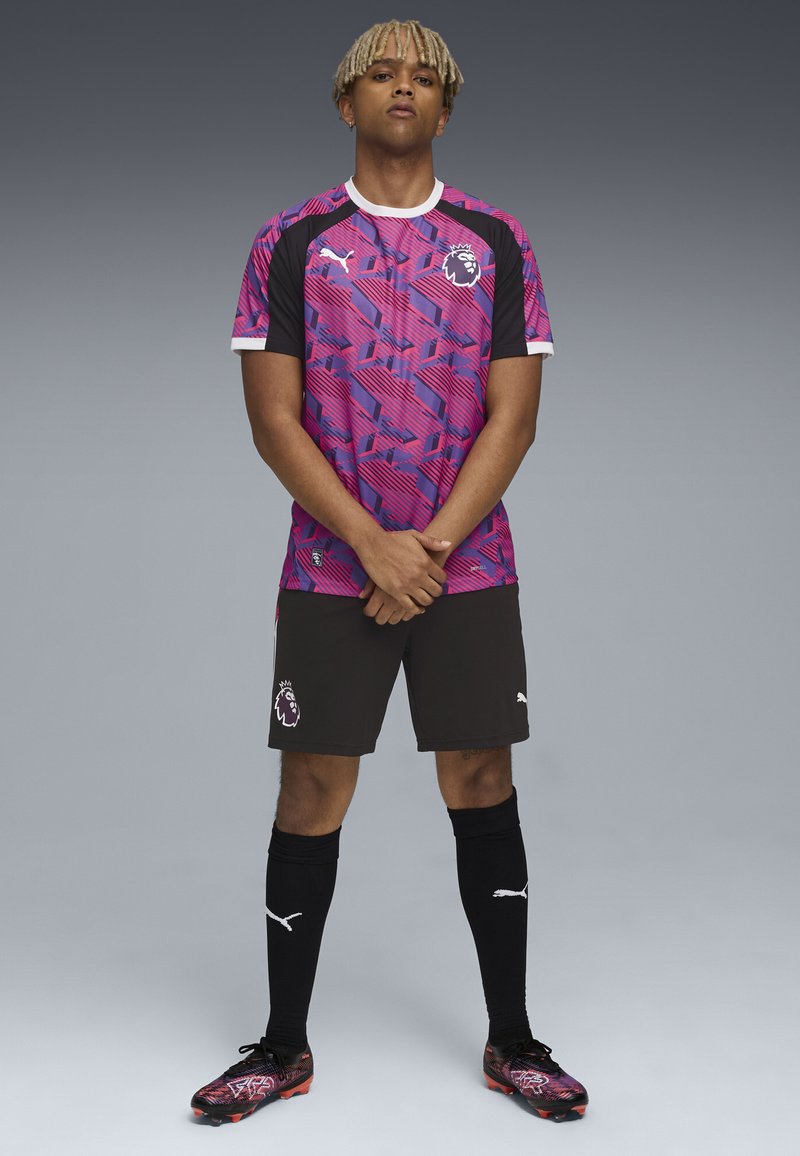 Echipamentul de fotbal Puma, care include un tricou cu un model roz și violet, pantaloni scurți negri și șosete asortate cu accente albe și logo-ul leului.