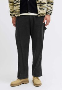 Sive hlače od kordura ravnog kroja, s teksturom okomitih rebrova, u kombinaciji s bež cipelama na vezanje i jaknom s uzorkom.