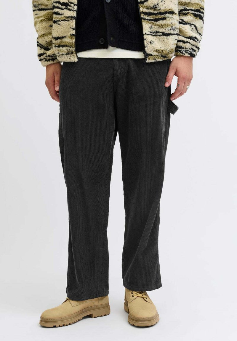 Sive hlače od kordura ravnog kroja, s teksturom okomitih rebrova, u kombinaciji s bež cipelama na vezanje i jaknom s uzorkom.