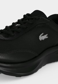 Baskets Lacoste noires avec dessus texturé, lacets noirs et petit logo crocodile argenté sur le côté.