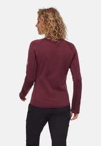 Maglietta a maniche lunghe bordeaux con una texture liscia, design aderente e maniche raglan. Presenta cuciture a contrasto e logo vicino al collo.