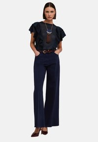 Granatowe spodnie szerokie w nogawkach połączone z ciemnoniebieską bluzką z falbanami na rękawach. Uzupełnione długim naszyjnikiem i brązowym paskiem.