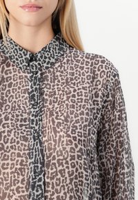 Camisa transparente com botão em padrão de pele de leopardo, apresentando um colarinho cinza-escuro e botões pretos, tecido texturizado com uma aparência leve e arejada.