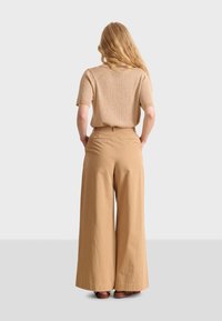 Pull court à manches courtes beige côtelé associé à un pantalon décontracté en toile kaki taille haute. Le pantalon présente une coupe large et une texture lisse.