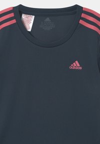 Camiseta deportiva de un oscuro color marino, hecha de material Primegreen, con acentos de tres rayas rosas en los hombros y un pequeño logo rosa en el pecho.