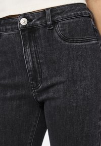 Črne denim hlače z gladko teksturo, z sprednjim žepom, srebrnim gumbom za zapiranje in rahlim zbledelostjo ob tkanini.
