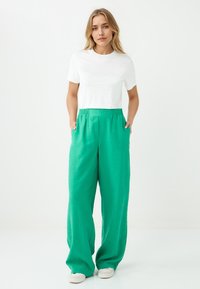 Witte crop top gecombineerd met loszittende, felgroene broek met elastische tailleband en zijzakken. Gladde stoftextuur.