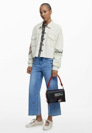 White cropped cord jacket with two front pockets, black graphic t-shirt underneath, light blue wide-leg denim, and black bag with red handle.