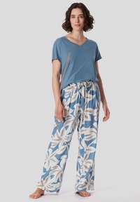 T-shirt in cotone blu con scollo a V abbinato a pantaloni larghi a fantasia con sfondo blu e disegni floreali bianchi con accenti beige e marroni.