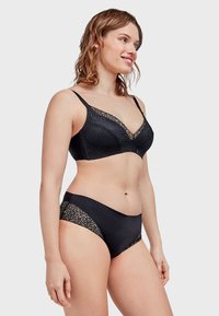 Soutien-gorge noir avec un bord en dentelle et des bretelles ajustables, accompagné de culottes noires avec des accents en dentelle. Les deux articles ont une texture lisse.