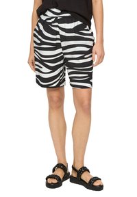 Czarno-białe spodenki w paski zebry z elastycznym paskiem w talii, z bocznymi kieszeniami i luźnym krojem, zestawione z masywnymi czarnymi sandałami.