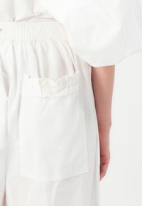 Garbiento in cotone bianco con tasca a forma di cuore con texture. Il design include una vita elastica e una texture morbida del tessuto.
