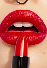 Bright red lipstick with a smooth, glossy finish held near full, plump lips. The lips have a defined outline and a rich texture.