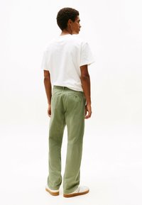 Pantaloni di cotone verde chiaro con un design a gamba dritta, indossati con una t-shirt bianca a collo rotondo e abbinati a sneaker bianche.