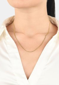 Guldfärgad kedjehalsband med en enkel länkdesign, som vilar eleganta på mjuk hud, i kombination med en vit skjorta med krage.