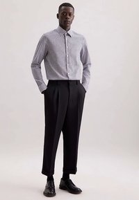 Camicia a quadri bianca e nera con bottoni abbinata a pantaloni neri a vita alta e scarpe nere, su uno sfondo neutro.