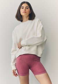 Sudadera blanca de gran tamaño con hombros caídos combinada con pantalones cortos de ciclismo ajustados y acanalados en color rosa. Combinación de moda sencilla e informal.