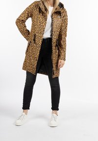 Leopardmönstrad regnjacka i brunt och svart, med huva, dragkedja fram och justerbara fästen. Bärs över svarta byxor och vita sneakers.