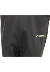 Sorte vandtætte bukser lavet af glat, slidstærkt materiale. Funktioner inkluderer en tætsiddende pasform og et grønt "ZIGZAG" logo på siden.