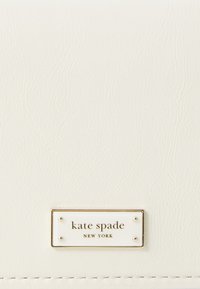 Biely kožený peňaženka s textúrovaným povrchom, zlatým kovovým hardvérom a značkovou platňou s nápisom "kate spade NEW YORK" v čiernej farbe.
