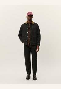 Dark denim jacket with a contrast corduroy collar, plaid shirt underneath, dark pants, and a maroon cap. Smooth texture with four pockets.