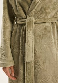 Jasnozielona polarowa szlafrok z teksturowanymi wzorami w kształcie muszli, z paskiem w talii i miękkim, puszystym materiałem. Zbliżenie na rękawy i detal z przodu.