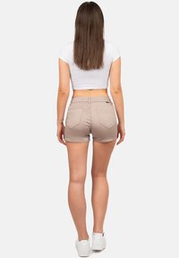 Beige denim shorts met een fitted ontwerp, voorzien van achterzakken en een iets afgerafelde zoom, gecombineerd met een witte crop top en witte sneakers.