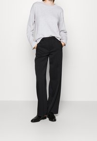 Pull en maille gris clair à manches longues, associé à un pantalon noir taille haute. Des chaussures noires complètent la tenue.