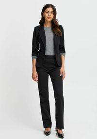 Black blazer with notch lapels, gray top, and black fitted trousers. The outfit features sleek lines and a tailored fit, complemented by black heels.