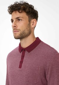 Polo a maniche lunghe bordeaux con un motivo strutturato, patta con tre bottoni e taschino sul petto. Tessuto morbido e colletto a contrasto.