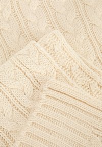 Tissu tricoté de couleur crème, présentant deux motifs : un tricot torsadé et une texture côtelée, mettant en valeur des dessins de points variés et des épaisseurs différentes.