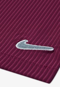 Burgundská športová tkanina s vertikálnou rebrovou textúrou; na jednej strane má vyšité šedé logo Nike swoosh.