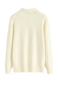 Pull oversize de couleur crème en tissu doux. Il présente un col à revers ainsi que des poignets et un ourlet côtelés, avec une texture lisse.