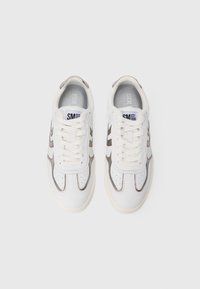 Ett par vita lädersneakers med beige detaljer, snören knutna och märkta inlägg, vy ovanifrån på en ljusgrå bakgrund.