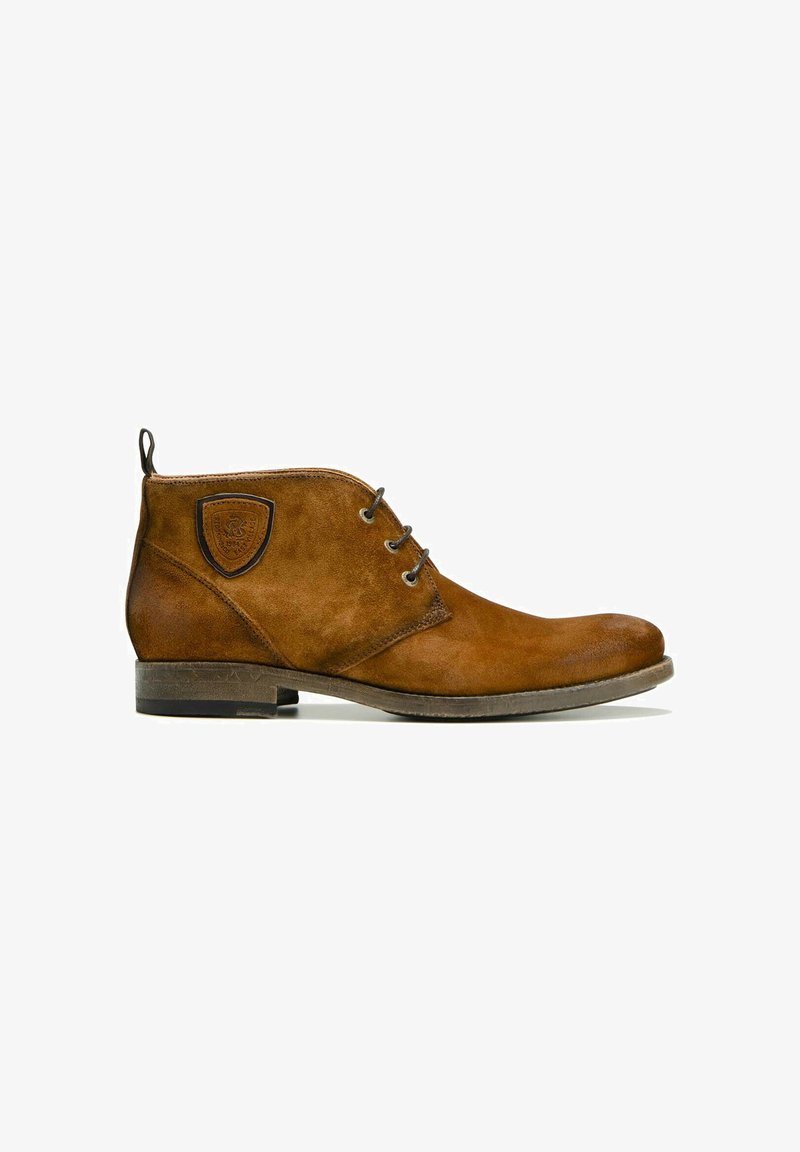 Bottine en suède marron avec trois œillets pour lacets, patch logo en cuir sur le côté, languette à l'arrière et semelle basse empilée.