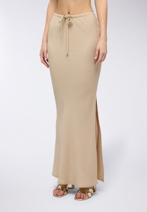 Gonna maxi beige con un motivo testurizzato, vita con coulisse e spacco laterale. Abbinata a sandali con tacco dorati.