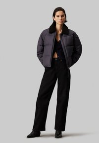 Pufferjack in donkergraad met een pluizige zwarte kraag, ritsluiting en puffy stiksels, gecombineerd met high-waisted zwarte broek en zwarte laarzen.