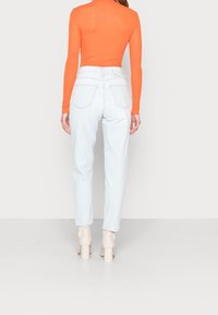 Jeans de tiro alto azul claro con un corte relajado, combinados con una blusa de manga larga naranja. Textura de denim suave y detalles mínimos.