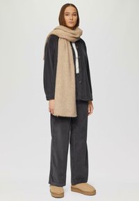 Ensemble en velours côtelé gris foncé avec coupe décontractée, comprenant un col roulé crème et une écharpe en laine beige. Accessoirisé avec des mocassins texturés marron clair.