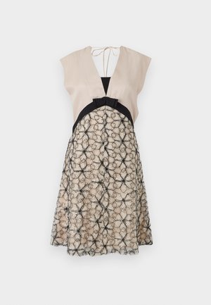 Robe beige sans manches avec un profond décolleté en V, accent noir à la taille et jupe crème texturée surmontée d'un motif floral noir rappelant une toile d'araignée.