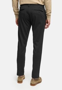 Pantalones de color gris oscuro con un corte ajustado, hechos de una tela suave. Cuentan con dos bolsillos traseros con botones y una cintura con trabillas.